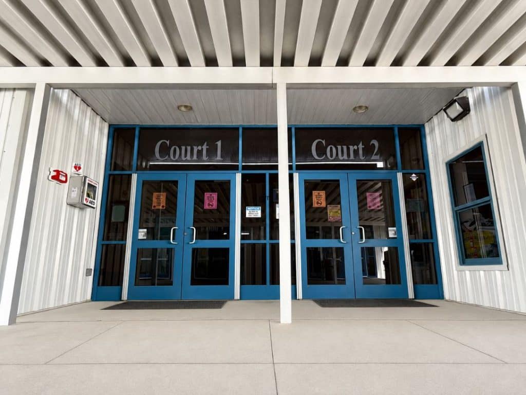 Entrance to two adjacent courts with blue-framed glass doors labeled Court 1 and Court 2 under a covered walkway.
